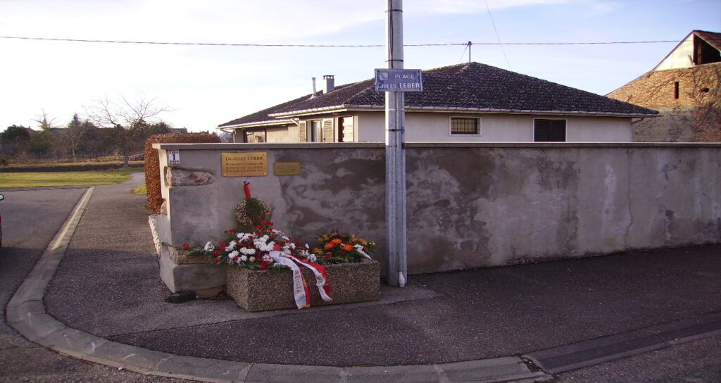 Mauer mit Erinnerungstafel für Julius Leber und dem Schild "Place Jules Leber" und einem Kranz sowie Blumen davor
