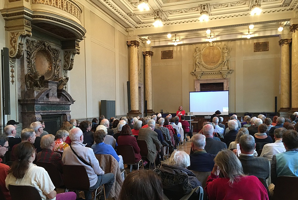 vollbesetzte Stuhlreihen im Saal