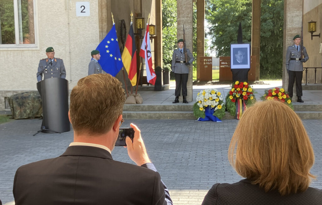 Soldate am Rednerpult neben Fahnen, Kränzen und einem Bild von Julius Leber